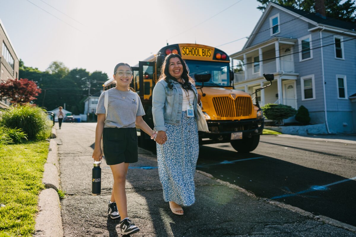 a woman and a young girl walk in front of a school bus